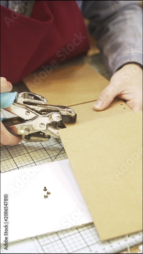 Person creating a scrapbook album and punching holes with tools