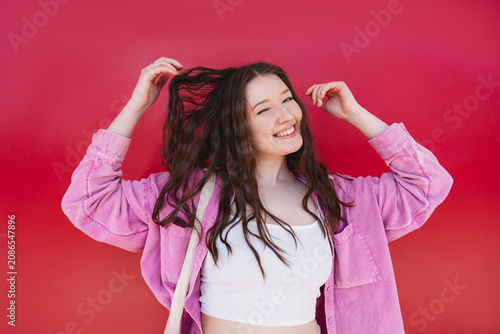 Smiling portrait of woman winking and touching hair against red background