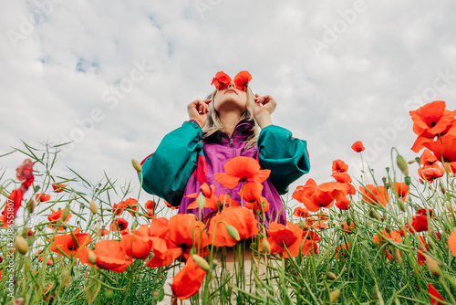 Woman in retro tracksuit covers eyes with red poppies in a meadow