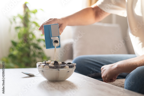 Quadro su tela Person's hand pouring plant-based milk from a carton into a bowl of cereal, repr