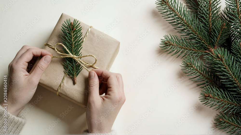 Hands wrapping a gift in brown paper with pine branch and gold ribbon