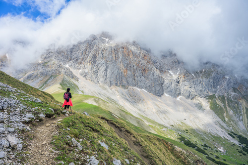 Female hiker admiring the dramatic view of the Wetterstein Mountains from the Predigtstuhl, majestic limestone peaks with clouds, alpine hiking in the German-Austrian Alps.