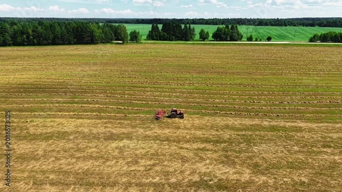 Red tractor harvesting hay in striped green and yellow agricultural fields under a clear sky