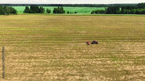 Tractor performing field preparation in large open farmland under clear skies in summer, aerial view