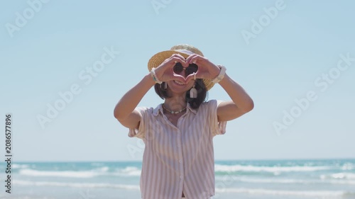 A happy young woman on the beach forms a heart shape with her hands, standing against the backdrop of the sea. a romantic mood.