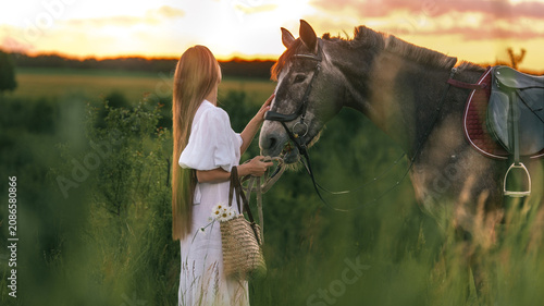 Foto Woman in white dress gently touching horse's face at sunset in a grassy field