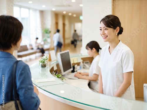 病院のカウンターで来院した患者に明るく対応する受付の女性