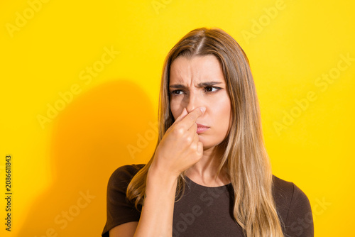 Valokuva Young woman holding her nose in disgust at a bad smell, portrait on a bright yel