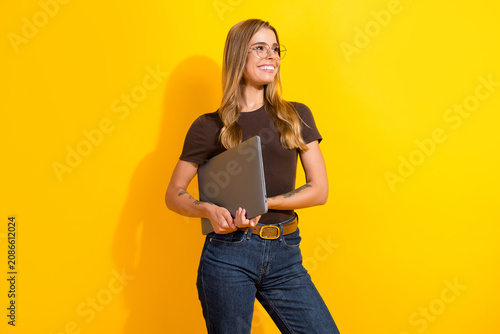 Fotografie Confident young woman holding a laptop and smiling against a bright yellow backg