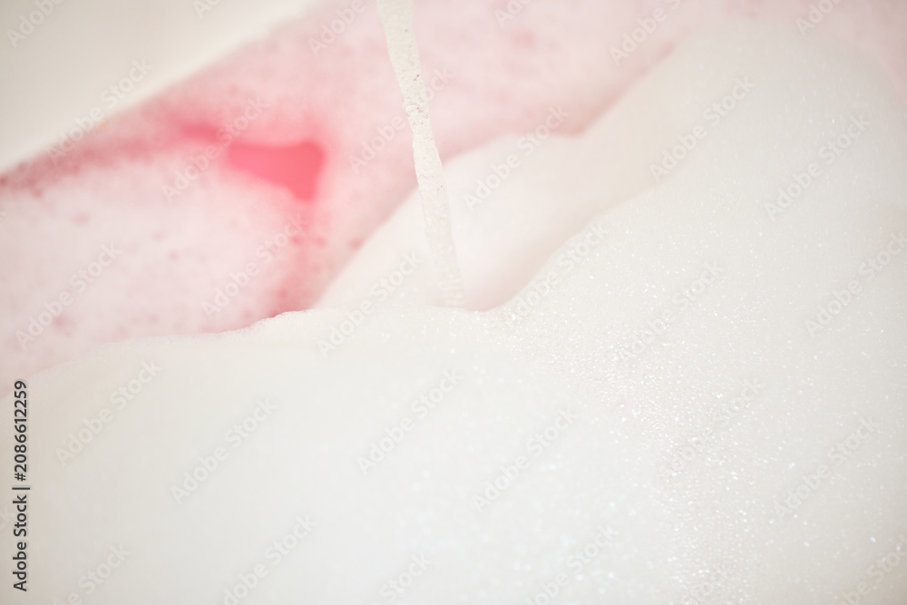 Fototapeta premium Water pouring into a bathtub, creating white foam and pink bubble bath for a relaxing spa and wellness experience