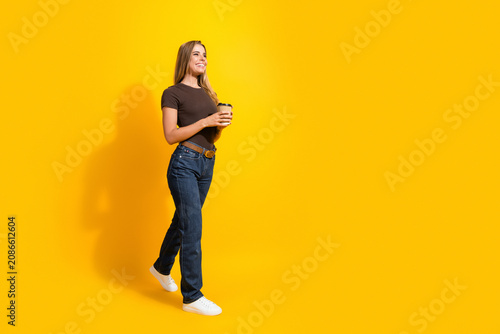 фотографія Smiling woman walking with coffee cup against bright yellow background in casual