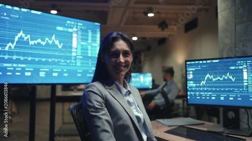 Side view Caucasian female trader using computer and mouse while watching financial charts. Woman broker analyzing stock market data in dark trading office. Professional working late at night.