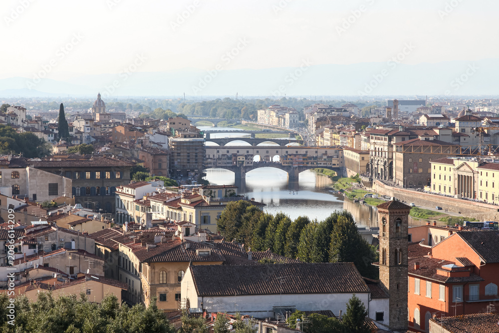 Fototapeta premium Elevated panoramic view of Ponte Vecchio crossing the Arno River in Florence, Tuscany, Italy, photographed in warm afternoon light with historic architecture and city skyline.