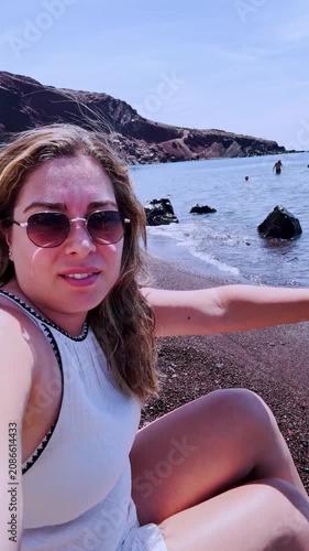 Beautiful smiling vlogger woman on santorini red beach, greece
