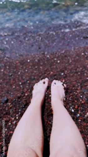 Woman's legs relaxing on santorini red beach in greece