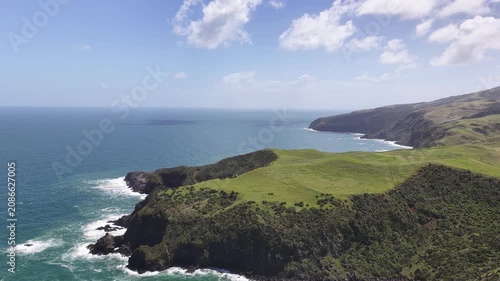 Aerial panorama of the rugged volcanic coastline on New Zealand's North Island, featuring dramatic sea cliffs, rolling green headlands, crashing Pacific waves and untouched coastal landscapes.