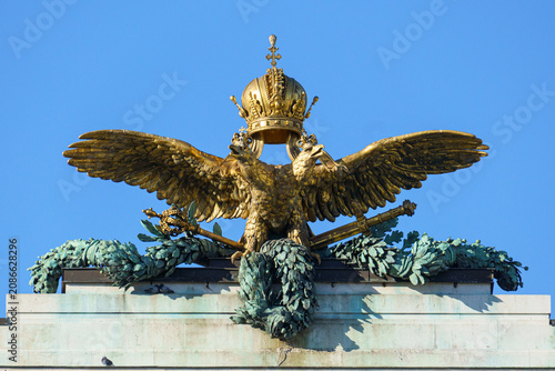 A detailed close up of the historic golden double headed eagle statue with the imperial crown on a classical building façade under a clear blue sky in Vienna, Austria.⁠