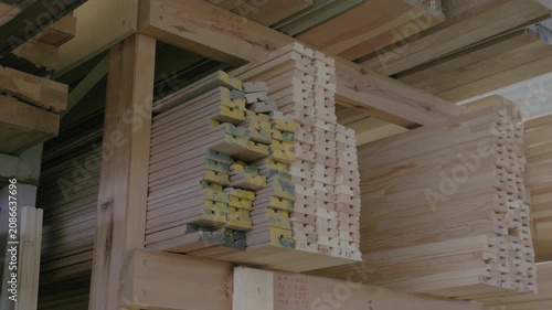 Stacked wooden profiles with marked measurements stored on factory shelving for window frame production