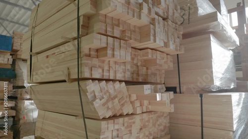 Stacked wooden profiles with marked measurements stored on factory shelving for window frame production