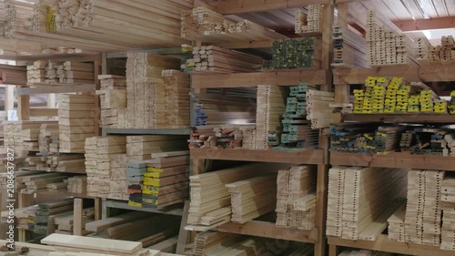 Stacked wooden profiles with marked measurements stored on factory shelving for window frame production