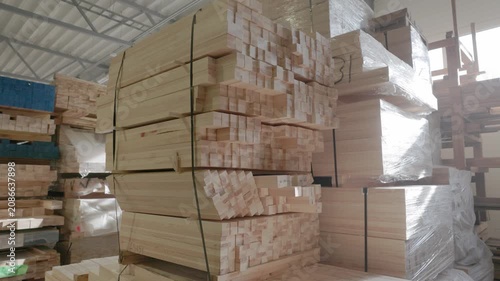 Stacked wooden profiles with marked measurements stored on factory shelving for window frame production