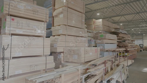 Stacked wooden profiles with marked measurements stored on factory shelving for window frame production