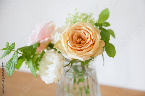 Foto ガラスの花びんに生けたオレンジ色と白色のバラとミントリーフ、さわやかなバラとグリーンの初夏のフラワーアレンジメント