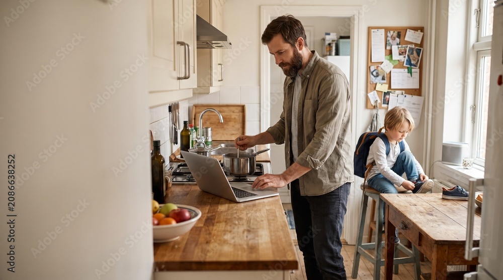Fototapeta premium Man working on laptop in modern kitchen with child nearby 