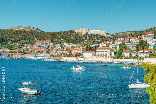 Photography Scenic view of Hvar town harbor with boats, red roof houses and hilltop fortress on Hvar Island, Dalmatia, Croatia