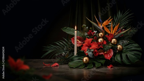 Elegant tropical flower arrangement with a glowing candle and golden ornaments creating a warm festive ambiance