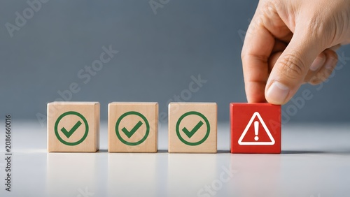 Hand selecting red block with warning triangle among green checkmark blocks representing quality control anomaly