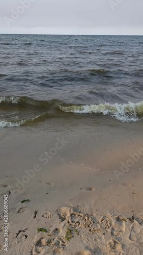 Vertical tilt-up shot of sea waves washing onto a sandy beach with footprints