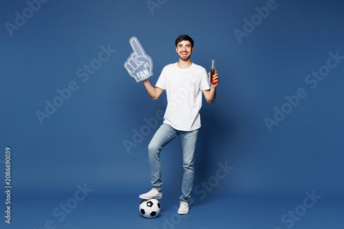 Obraz na plátne Full body young man fan wear white t-shirt foam 1 fan glove finger up drink beer