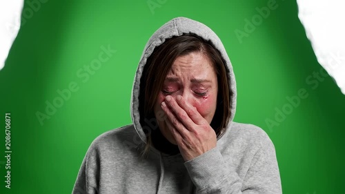 Emotional woman in a grey hoodie crying against a green screen. Expressing deep sadness, grief, and despair, perfect for dramatic storytelling and mental health awareness content.