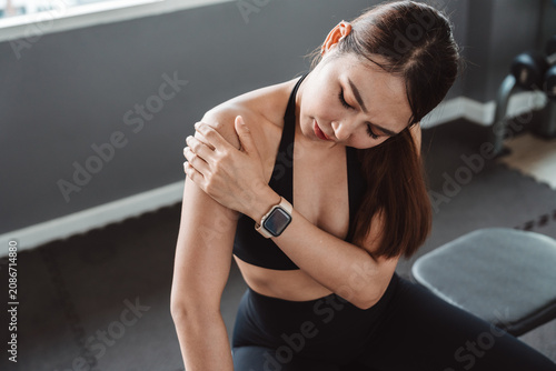 Obraz na plátně Fitness woman suffering from shoulder pain after strength training in gym, showing muscle strain, sports injury, healthcare, rehabilitation, recovery and active wellness lifestyle concept