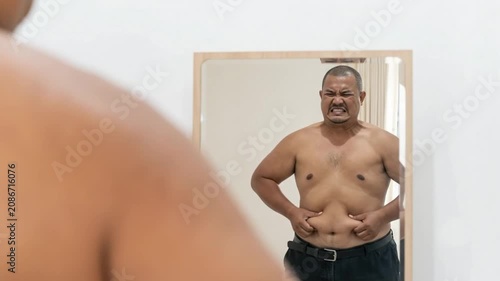 Overweight Man Looking in Mirror and Pinching Belly Fat