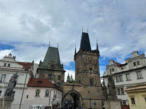 The Gothic Lesser Town Bridge Tower stands at the entrance to Charles Bridge in Prague. Historic architecture and a stone archway sit under a cloudy sky.