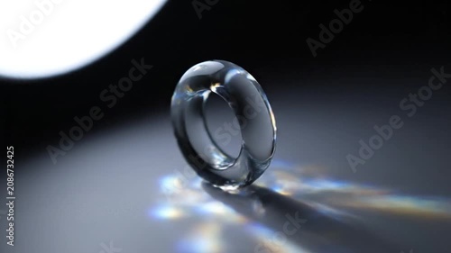 A clear glass ring casting beautiful rainbow light refractions on a dark surface.
