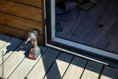 Quadro em tela Cordless impact driver on wooden deck at private house entrance, sunny outdoor workspace