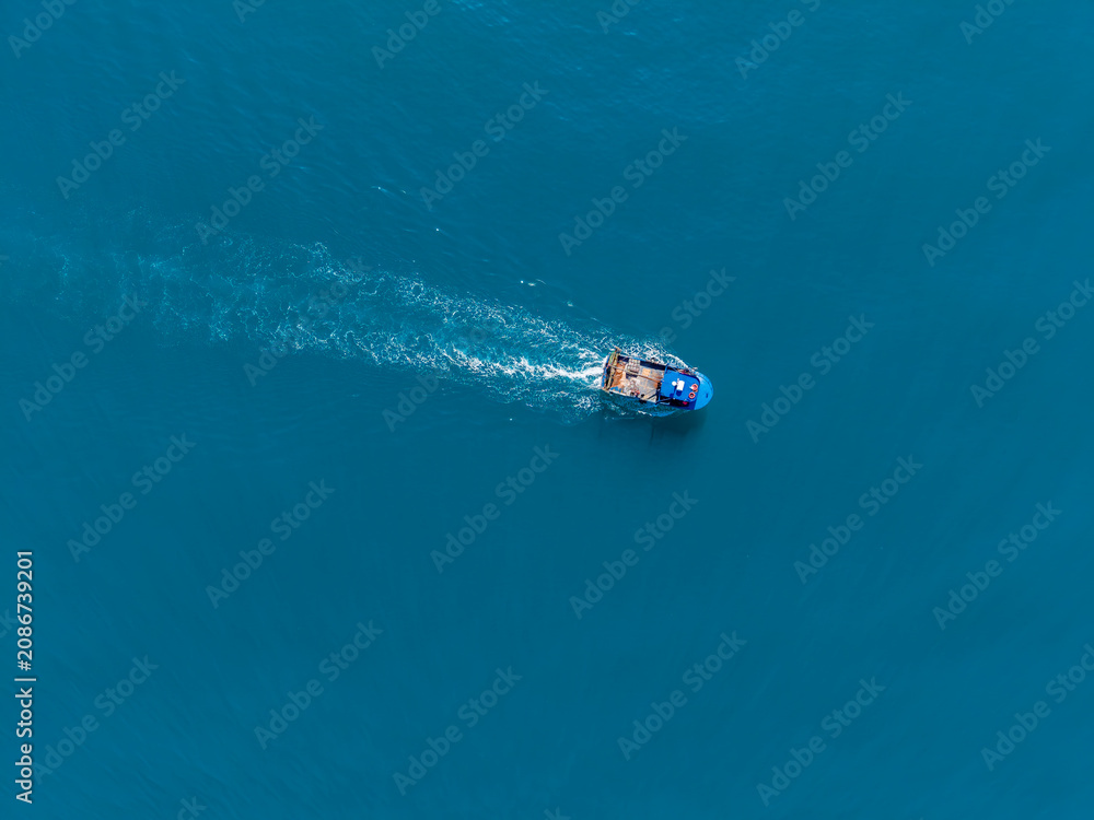 Naklejka premium Boat travels over clear blue water in a vast ocean, creating ripples as it moves under sunlight during a warm day in summer