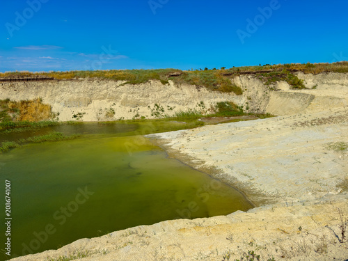 Green water fills a low area between beige cliffs under a blue sky in a landscape during daytime with clear visibility