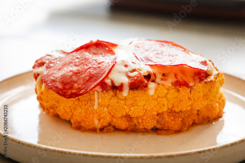 Close-up of a golden-baked cauliflower steak pizza, layered with rich tomato sauce, melted mozzarella cheese, and crispy salami slices on a baking sheet