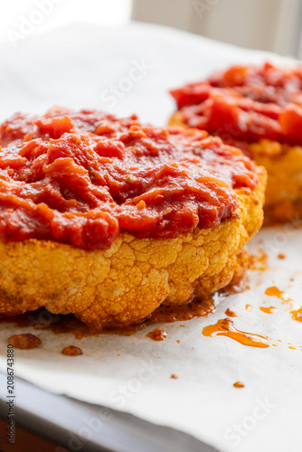Close-up of golden roasted cauliflower steaks baked in a sheet pan, smothered with rich herb tomato sauce