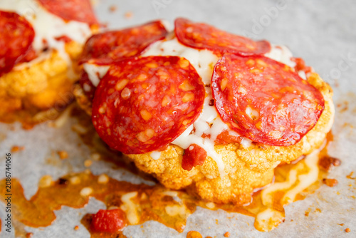 Close-up of a golden-baked cauliflower steak pizza, layered with rich tomato sauce, melted mozzarella cheese, and crispy salami slices on a baking sheet