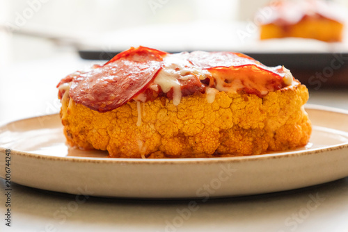 Close-up of a golden-baked cauliflower steak pizza, layered with rich tomato sauce, melted mozzarella cheese, and crispy salami slices on a baking sheet