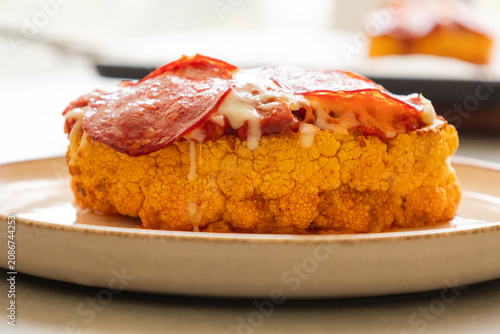Close-up of a golden-baked cauliflower steak pizza, layered with rich tomato sauce, melted mozzarella cheese, and crispy salami slices on a baking sheet