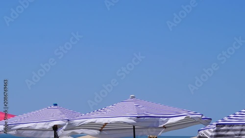 Blue and white striped beach umbrellas against a clear bright summer sky.