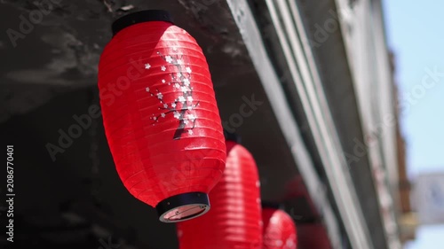 Red paper lantern with cherry blossom print hanging outdoors.