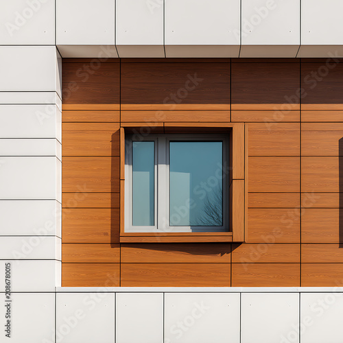 Modern building facade featuring geometric wood paneling and white composite tiles with a central window reflecting the clear sky in a contemporary architectural design