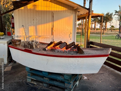 Traditional boat barbecue with sardines grilling over charcoal fire at sunset in a beach restaurant